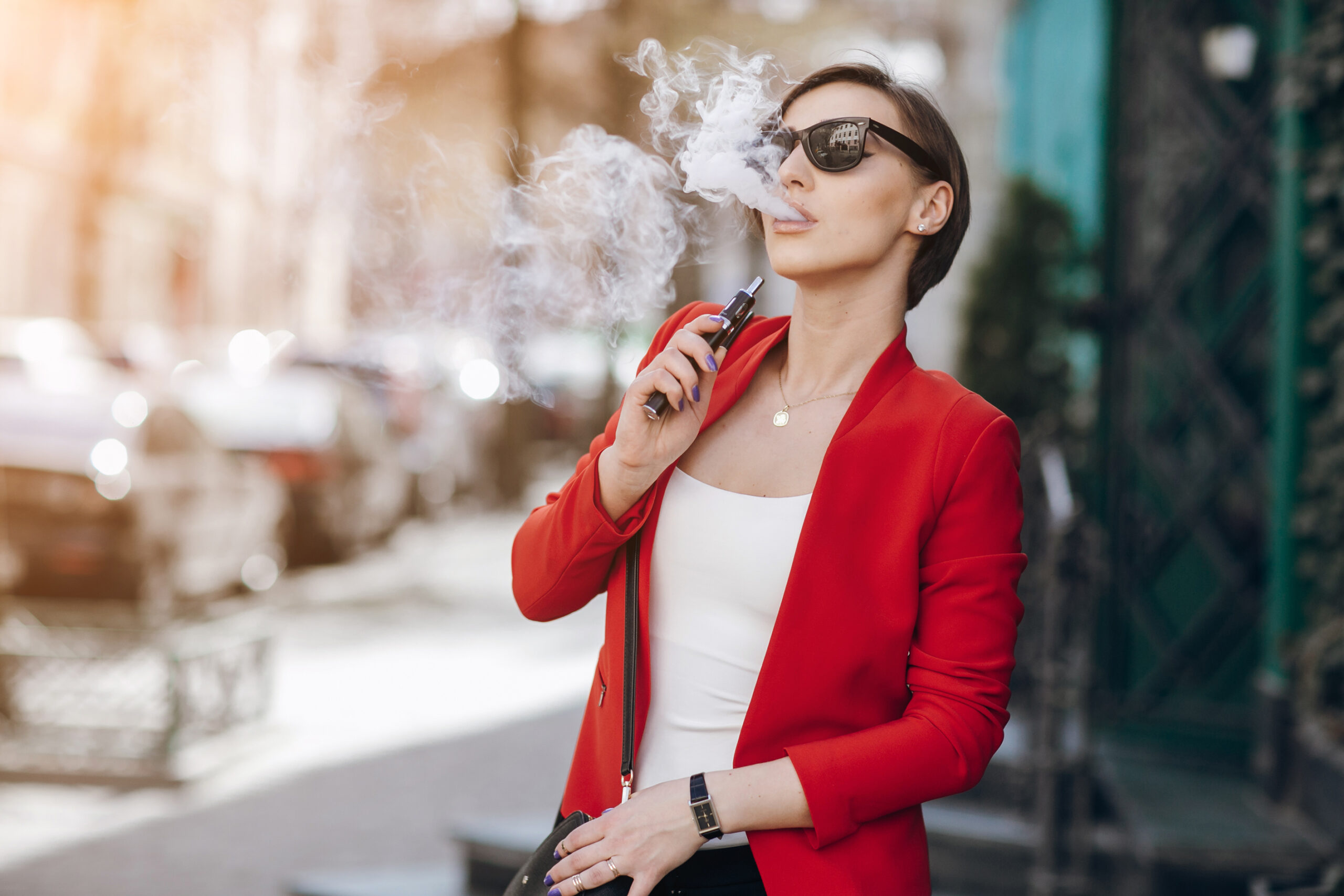 spectacular young brunette outside uses fashionable and healthy e-cigarette